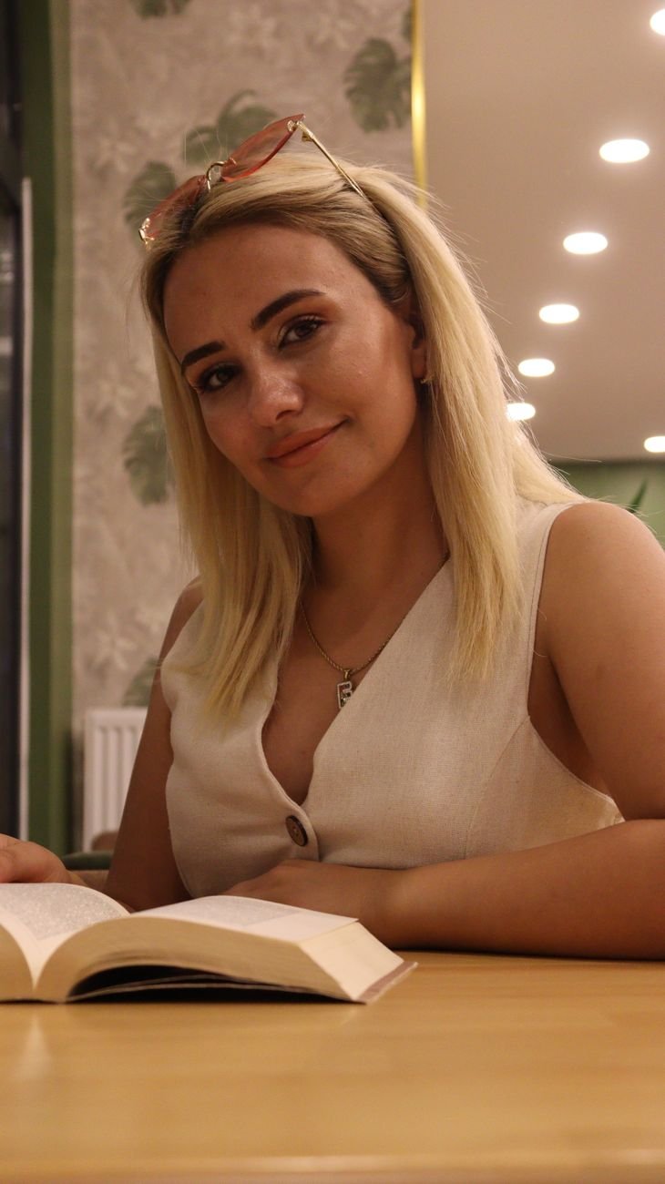 A young woman reads a book indoors under warm lighting